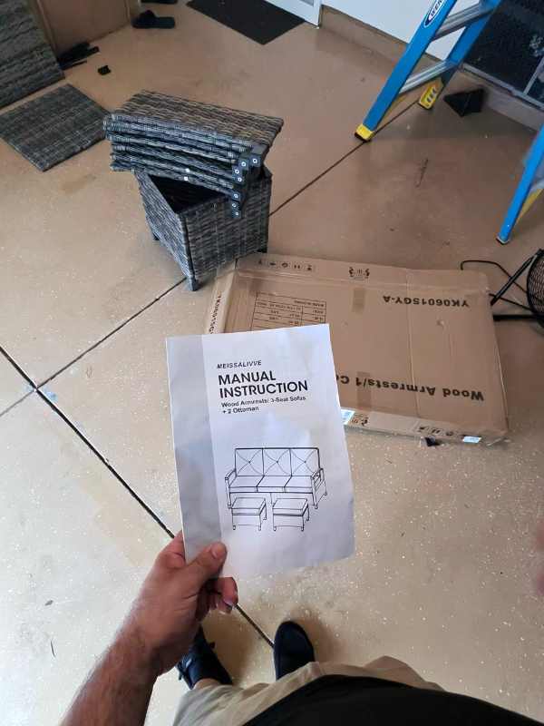 Instruction manual held beside patio furniture frame parts and opened packaging.