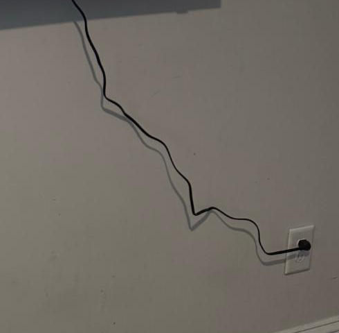 Black TV power cord running down a light-colored wall to a nearby outlet.