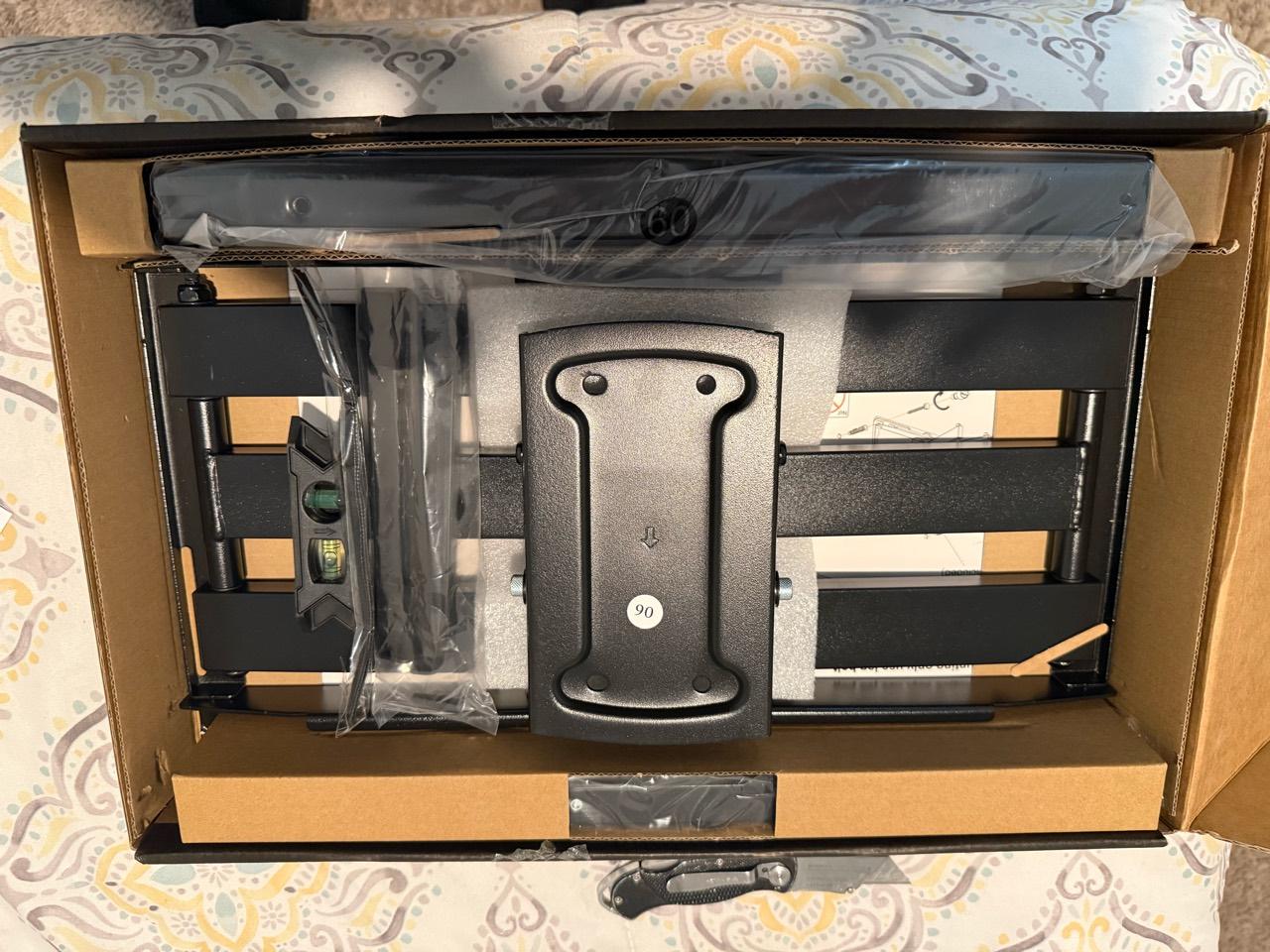 Black TV-mount hardware and mounting rails in an open cardboard box.