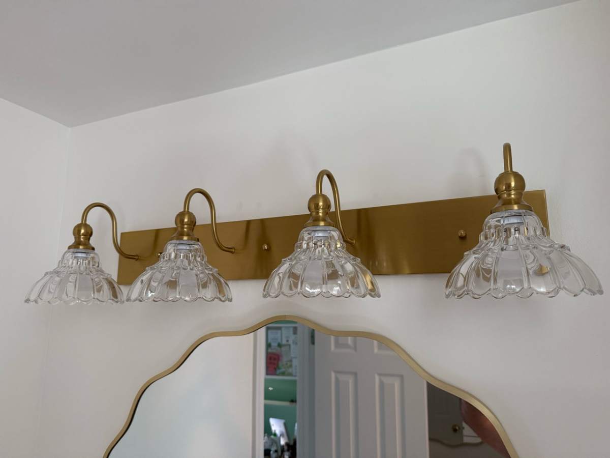 Wall-mounted vanity light with four clear glass shades above a bathroom mirror.