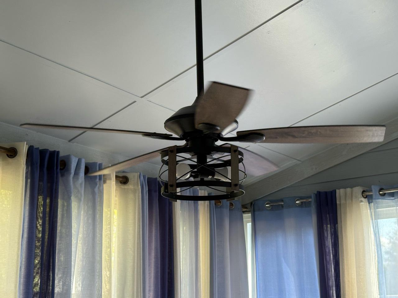 Close-up of a dark ceiling fan with wood-tone blades and a cage-style light kit; the ceiling mounting area is outside the frame.